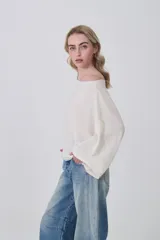 Sweater holgado de tejido ligero, color beige claro, con escote asimétrico que deja un hombro al descubierto.