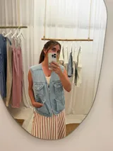 Chaleco de jean celeste con cierre frontal y múltiples bolsillos con botón.