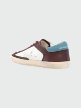 Zapatillas Golden Goose modelo Super Star, de cuero color marrón y blanco, con estrella negra en el lateral y detalles en celeste.