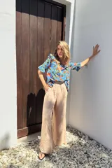 Blusa celeste con estampado floral en tonos naranja, verde y marrón. Tiene escote redondo y mangas cortas con volados.