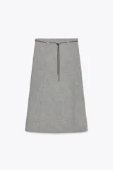Falda midi de lino color gris con textura. Tiene tiro alto, cinturón fino del mismo tejido y abertura frontal. Cierre lateral con cremallera oculta.