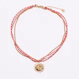 Collar de tres tiras, dos de hilo trenzado rojo y naranja, y una de cadena dorada. Incluye un dije colgante dorado con el diseño de un sol con rostro humano y una luna en su interior.