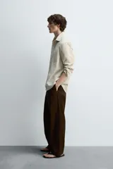 Camisa de hombre relaxed fit confeccionada en tejido de algodón a rayas verticales color beige y marrón. Tiene cuello solapa, manga larga con puños abotonados, bolsillo de parche en el pecho y cierre frontal con botones.