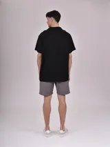 Camisa de manga corta con estampado de hojas color verde sobre fondo beige, cuello solapa y bolsillo en el pecho.