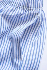 Short de baño celeste con rayas verticales blancas, cintura elástica con cordón ajustable, bolsillos laterales y trasero con cierre, logo de la marca bordado en la pierna.