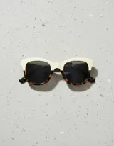 Lentes de sol cuadrados con armazón bicolor: parte superior color crema y parte inferior con estampado carey. Lentes polarizados negros con protección UV400.