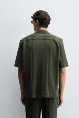 Camisa verde militar de corte relaxed fit, con cuello bowling, manga corta, bajo con aberturas laterales y cierre frontal de botonadura.