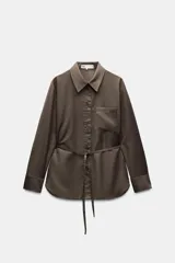 Camisa marrón de Zara Woman Collection confeccionada en hilatura con viscosa, de cuello solapa y manga larga acabada en puño. Presenta un bolsillo de plastrón en el pecho, cinturón en mismo tejido ajustable con lazadas y bajo asimétrico.