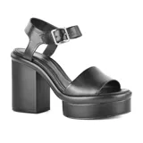 Sandalias negras de cuero sintético con plataforma y taco cuadrado alto. Tira ancha sobre los dedos y pulsera con hebilla al tobillo.