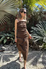 Vestido marrón de tirantes finos con frunces en el busto y falda midi con corte irregular.