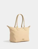 Bolso tipo shopper color beige con doble asa corta de hombro, cierre superior y tag de goma con logo.