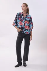 Camisa de mangas 3/4 con estampado floral en tonos naranja, celeste y verde sobre fondo negro.