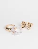 Set de tres anillos dorados: uno liso, uno transparente con un corazón dorado y uno con forma de moño.