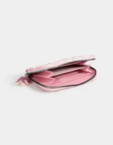 Billetera pequeña de cuerina color blanco con estampado de lazos rosas y corazones. Tiene cierre circundante y tirador de goma.