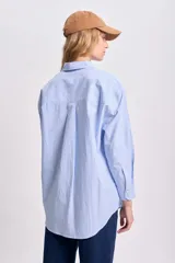 Camisa celeste con rayas verticales blancas, de corte holgado, manga larga y cuello clásico.