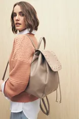 Mochila negra de símil cuero texturizado con tapa en acabado gamuzado, decorada con apliques de tachas metálicas. Tiene asa superior y correas regulables.