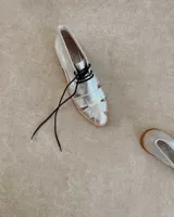 Zapato acordonado plateado de cuero vacuno con diseño calado y cordones negros.