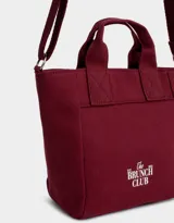 Cartera mini de lona color crudo con estampado "The Brunch Club" en azul marino. Tiene correa regulable y desmontable, manijas superiores y cierre superior.