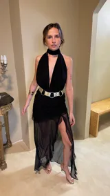 Vestido largo de microtul color rojo, con escote profundo en V y cuello halter. La falda presenta un diseño con frunces, transparencias y un tajo lateral pronunciado con detalle de volados.