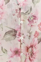 Camisa semitransparente con estampado de flores en tonos rosa y verde, cuello pico y manga larga con puños. Tiene aberturas laterales y cierre frontal con botones.