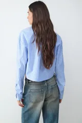 Camisa celeste a rayas verticales blancas, de popelina asimétrica y manga larga.
