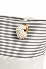 Bolso de tela tipo tote bag con estampado de rayas horizontales azules y blancas, y base de color beige. Tiene asas de cuerda de color beige.