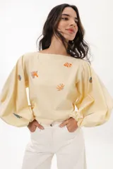 Blusa color crema de algodón con escote a la base y mangas abullonadas. Presenta bordados artesanales de motivos marinos en tonos naranja y azul.