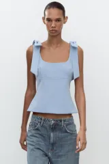 Top blanco de tejido elástico con escote cuadrado y tirantes con lazos decorativos. Tiene forro interior y cierre lateral con cremallera oculta.