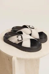 Sandalias planas color beige con tiras cruzadas y hebilla decorativa.