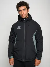 Campera corta de abrigo Umbro Crafted Pro, color negro con paneles laterales en gris. Presenta capucha con cordón ajustable, cierre frontal completo y logo de la marca bordado en el pecho.