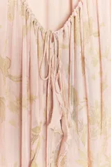 Vestido largo de gasa color rosa pálido con estampado floral en tonos dorados, escote en pico ajustable con lazada, mangas largas abullonadas con elástico y volantes en los puños, forro interior y bajo con volantes escalonados.