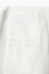 Pantalón de vestir blanco de tiro alto, con cierre, botón oculto y corchete. Presenta bolsillos al bies, bolsillos decorativos atrás y piernas amplias con pliegues adelante y atrás. Confeccionado en tejido liviano de mezcla de lino y viscosa.