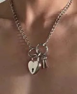 Collar plateado con cadena de eslabones gruesos, dije de candado en forma de corazón y dos llaves.