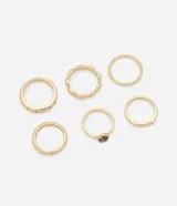 Set de seis anillos rígidos con baño de oro claro. El conjunto incluye un anillo con pequeños cristales incrustados, uno con borde ondulado, uno con textura en relieve, uno con detalle de flor en abulón y dos anillos lisos de diseño minimalista.