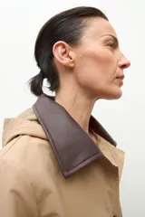 Abrigo tipo trench largo color beige, con cuello de contraste en material oscuro (posiblemente cuero o efecto cuero). Presenta cierre frontal con botones y corte recto.