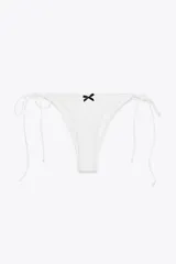 Braguita de bikini blanca de tiro medio, con cintura ajustable con lazos laterales. Presenta un volante frontal y un lazo negro en el centro.