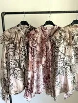 Camisa de seda italiana con estampado sutil de animal print en tonos neutros y rojizos. Presenta cuello con lazo ajustable y volados en el frente y puños elásticos.