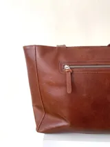 Cartera tipo tote de cuero graneado color negro, con textura uniforme y suave al tacto. Tiene manijas de 55 cm, bolsillo frontal con broche imantado, bolsillo trasero con cierre metálico, cierre principal metálico, forro interior y tres bolsillos internos (uno con cierre, uno plaqué y uno tipo sobre con solapa y botón).