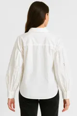 Camisa celeste de algodón con cuello camisero, mangas largas abullonadas con bordados y cierre frontal con botones.