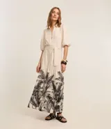 Vestido chemise evasé midi de viscolino color crema, con mangas abullonadas cortas, cuello camisero, botones delanteros, cinturón tejido para lazo en la cintura y bajo fruncido con estampa de palmeras y follaje.