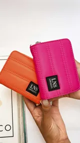 Billetera corta con cierre alrededor y tapa, confeccionada en tela capitoneada. Incluye varias reparticiones con tarjeteros y bolsillos internos, y una correa de mano desmontable. Disponible en negro, rojo y dorado.