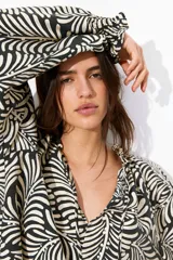 Blusa oversized con estampado de hojas en blanco y negro, cuello con volados y lazos, mangas largas raglán con puños elásticos y bajo redondeado.