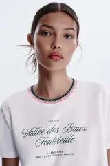Camiseta blanca de algodón con cuello redondo y detalle de tricot a contraste en azul marino. Estampado frontal con texto "Estate sulla Costiera Amalfitana" en azul marino.