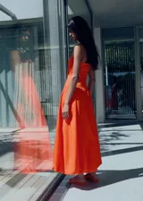 Vestido midi naranja con corpiño ajustado tipo palabra de honor y tirantes finos. La falda es de corte globo con volumen y frunces en la cintura.