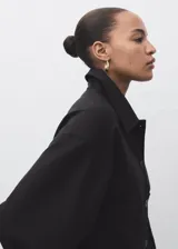 Chaqueta corta de color negro, con cuello camisero, cierre frontal de botones y bolsillos de parche.