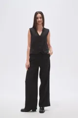 Chaleco negro con finas rayas verticales blancas (pinstripe), escote en V y cierre frontal de botones. Presenta bolsillos ribeteados en la parte inferior delantera.