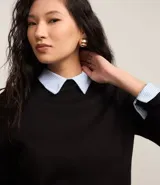 Sweater negro de punto con cuello redondo, puños y ruedo acanalados. Incluye cuello, puños y ruedo de camisa celeste a rayas.