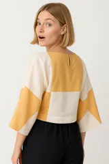 Blusa corta con diseño geométrico en tonos beige y mostaza, de corte holgado y mangas 3/4.