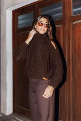 Sweater marrón de lana gruesa con cuello alto y hombros descubiertos, unidos por una tira con hebilla metálica.