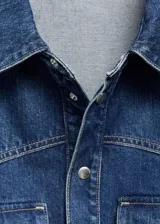 Camisa de jean azul con bolsillos de solapa en el pecho, manga larga con puños abotonados, diseño recto y oversize, cuello camisero y cierre delantero con botones.